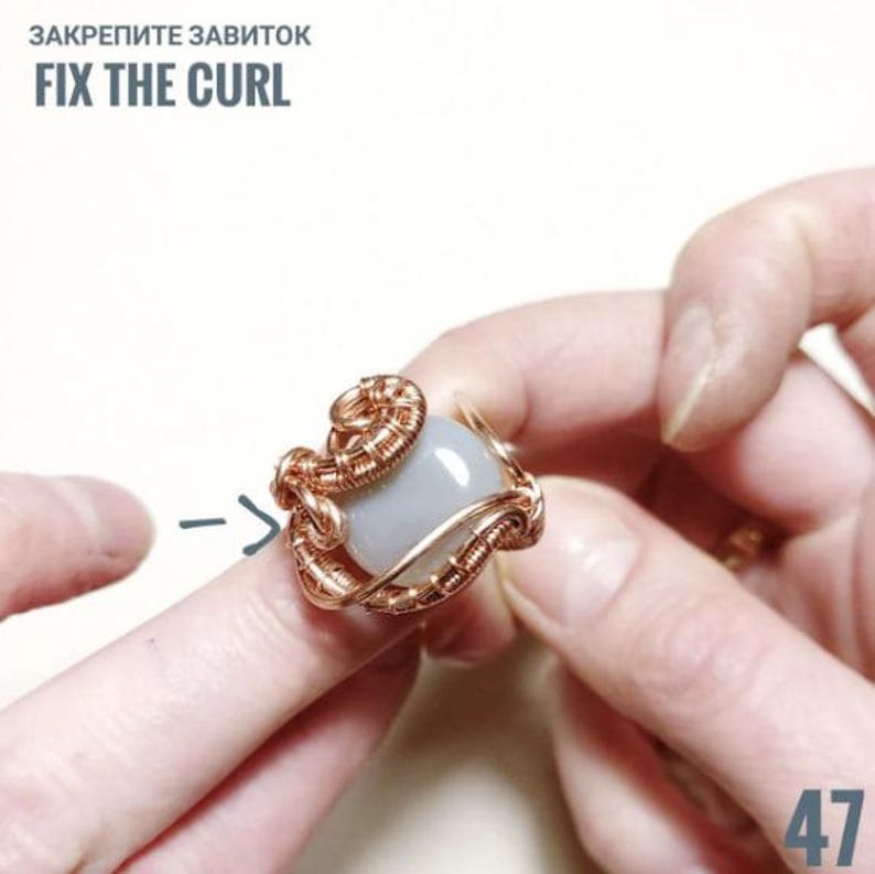 Peut inclure: Une bague en fil de cuivre avec une pierre bleu clair. La bague pr&eacute;sente un travail de filigrane complexe et le texte "FIX THE CURL". La bague est tenue par les doigts d'une personne.