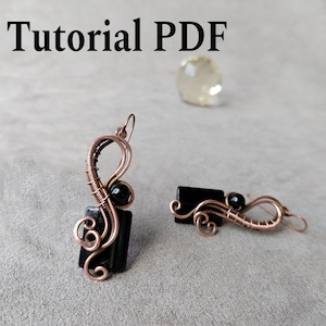 Può includere: Orecchini fatti a mano con filo di rame, perline nere e una pietra rettangolare. Gli orecchini hanno un design unico e artigianale. Il testo "Tutorial PDF" è visibile.