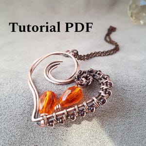Może przedstawiać: Ręcznie robiony wisiorek z drutu miedzianego w kształcie serca, z pomarańczowymi kryształkami i ciemnym łańcuszkiem. Wisiorek ma czarny napis "Tutorial PDF".
