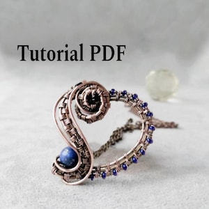Puede incluir: Un colgante artesanal de alambre de cobre con un diseño en espiral, con una piedra preciosa azul y pequeñas cuentas azules. El colgante está unido a una cadena. El texto "Tutorial PDF" se muestra arriba.