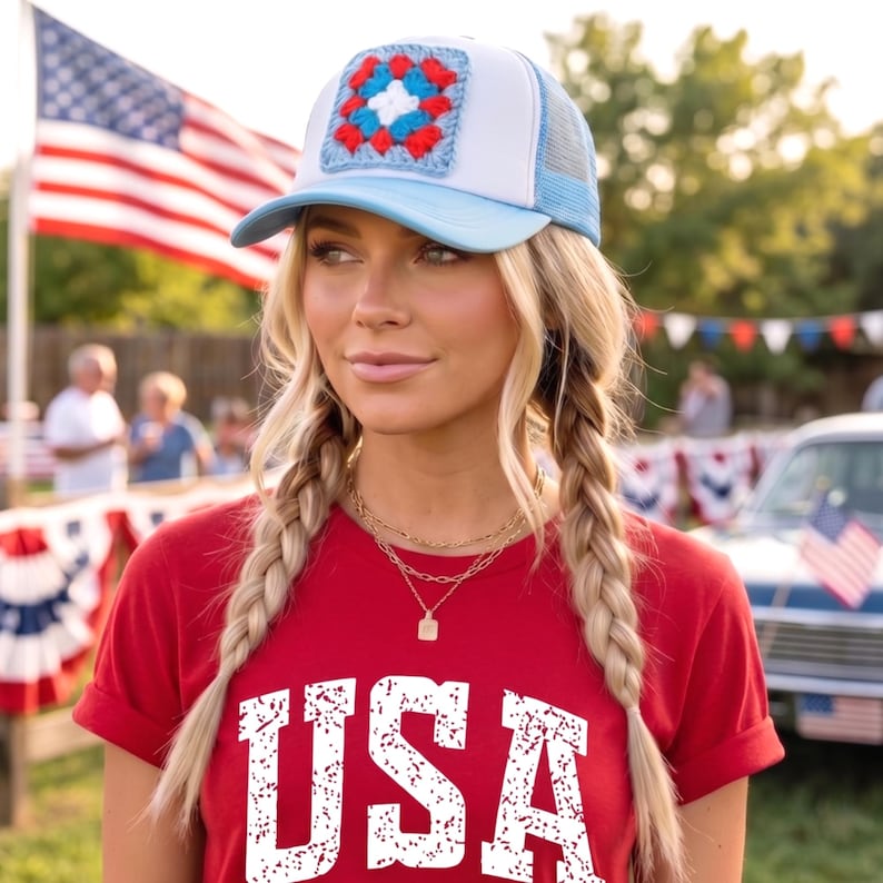 May include: A light blue and white trucker hat with a crocheted square design in red, white, and blue. The hat is worn with a red t-shirt with the word "USA" printed in white.