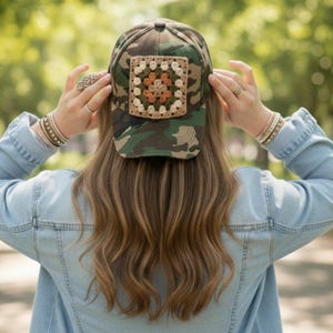 May include: Camouflage baseball cap with a square, crocheted patch in shades of cream, brown, and green. The cap features a classic six-panel design and a curved brim. The patch is centered on the front of the cap.