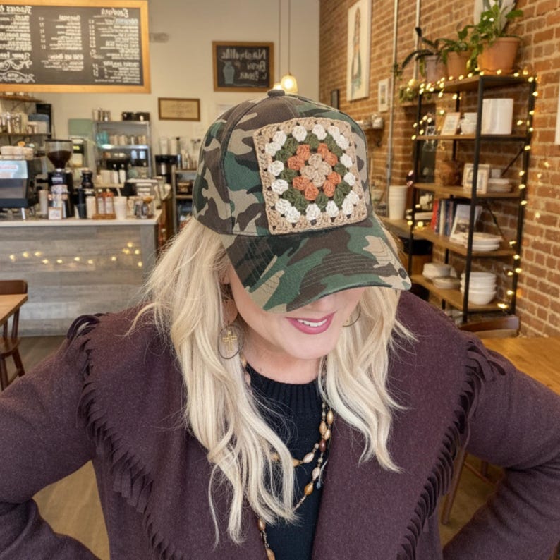 May include: Camouflage baseball cap with a square, crocheted patch in shades of beige, orange, and green. The cap features a classic six-panel design and a curved brim. The hat is a stylish accessory.
