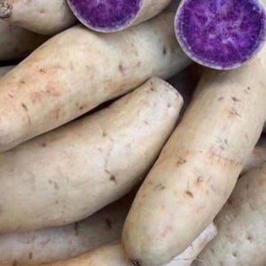 May include: Close-up of several purple sweet potatoes, with a few cut open to reveal the vibrant purple flesh. The potatoes have a light brown skin and are arranged in a pile.