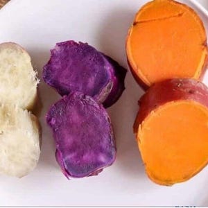 May include: A white plate holds sliced sweet potatoes. The sweet potatoes are cut in half, revealing the orange, purple, and white flesh. The skin of the sweet potatoes is a reddish-brown color.