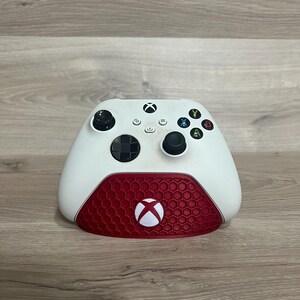 Può includere: Un controller Xbox bianco e rosso. La metà superiore è bianca con pulsanti neri e un D-pad nero. La metà inferiore è rossa con un motivo a nido d'ape e il logo Xbox.