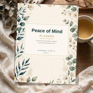 May include: A rectangular planner titled Peace of Mind PLANNER with the subtitle An end-of-life & emergency organizer for you and the people you love. The cover features a cream background with green leaves and white flowers along the edges.