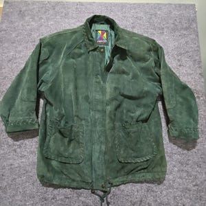 May include: A dark green suede jacket with a button-down front, two front pockets, and a drawstring waist. The jacket has a collar and long sleeves with decorative stitching on the cuffs. The label reads "KONITOR" with a colorful logo.