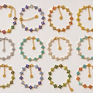 May include: Twelve gold-tone chain bracelets arranged in a grid, each featuring a series of four-petaled flower charms set with sparkling crystals in various colors including red, blue, yellow, green, orange, white, and multi-colored combinations.