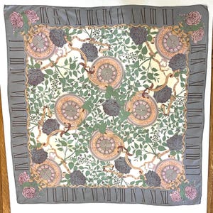 May include: Square silk scarf with a gray border featuring Roman numerals. The scarf has a cream background with clocks, roses, and foliage in shades of pink, gray, and green. Decorative ribbons and floral arrangements are also present.