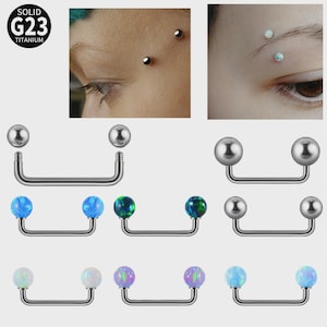May include: Solid G23 titanium eyebrow piercings. The image shows several curved barbell piercings with a variety of ball colours, including silver, blue, green, and purple. The piercings are displayed with close-up images of the piercings on an eyebrow.