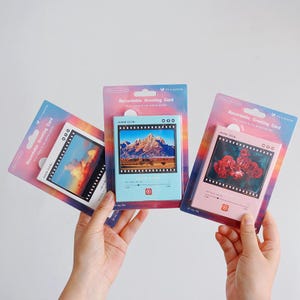 Könnte beinhalten: Eine weiße Keramik-Tasse mit schwarzem Henkel und dem Text "But First, Coffee" in fetter, schwarzer Schrift. Die Tasse steht vor einem verschwommenen Hintergrund, der eine gemütliche Umgebung suggeriert.