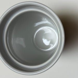 May include: Overhead view of a gray ceramic mug. The mug has a smooth, glossy finish and a simple, minimalist design. The interior is a lighter shade of gray, and the mug is empty.