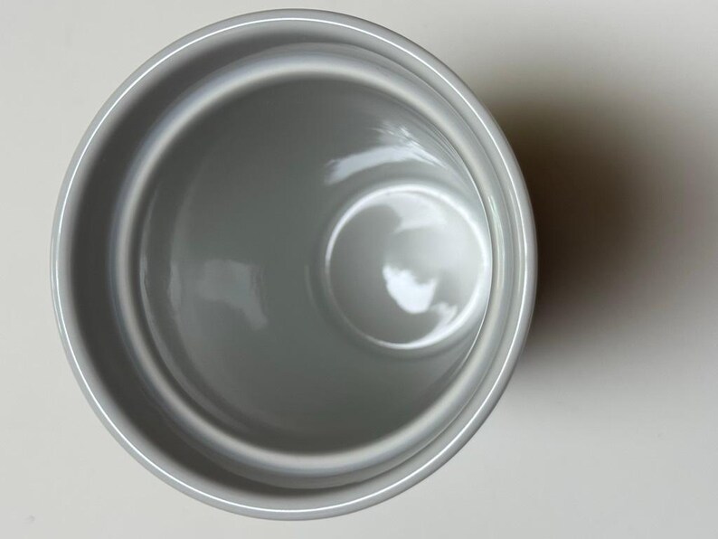 May include: Overhead view of a gray ceramic mug. The mug has a smooth, glossy finish and a simple, minimalist design. The interior is a lighter shade of gray, and the mug is empty.