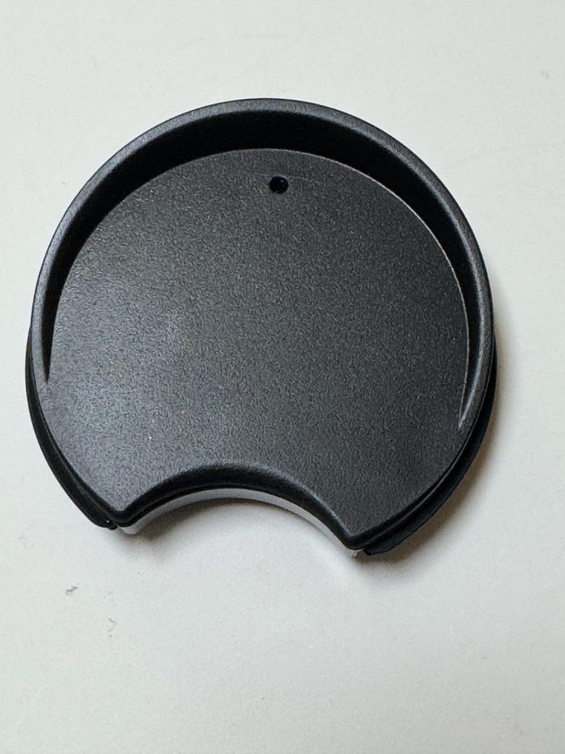 May include: A black, semi-circular lid with a small hole, likely for a travel mug or cup. The lid has a textured surface and rounded edges, with a design reminiscent of mouse ears.