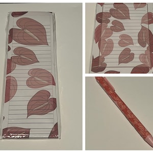 May include: A set of lined notepads and a pen. The notepad has a white background with a pattern of pinkish-red heart-shaped leaves. The pen is pinkish-red with a matching leaf pattern. The notepad is wrapped in clear plastic.