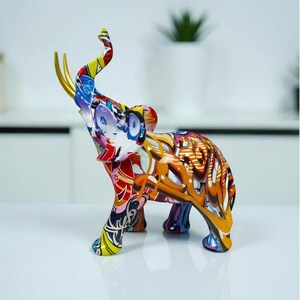 Peut inclure: Figurine d'éléphant colorée avec une trompe levée et des défenses dorées. L'éléphant est décoré d'un mélange vibrant de motifs et de couleurs, dont le rouge, le bleu, le jaune et l'orange. C'est un objet décoratif.