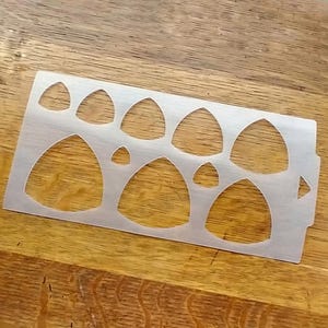 May include: A clear plastic stencil with multiple teardrop shapes of varying sizes. The stencil is designed for crafting and creating projects.