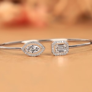 May include: A silver bracelet with two diamond-studded settings. One setting is a marquise shape, and the other is a square shape. The bracelet is on a neutral background.