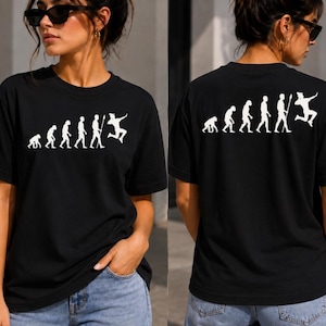 May include: A black short-sleeved t-shirt featuring a white graphic print on the front and back. The design depicts the evolutionary progression of primates, culminating in a figure performing a dynamic jumping pose with a staff in hand.