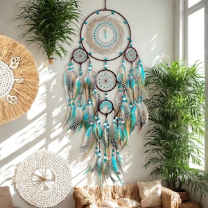 May include: A large, handcrafted dreamcatcher with a brown frame and multiple circular designs. The dreamcatcher features turquoise beads and feathers in shades of blue, brown, and white. It is a decorative wall hanging, perfect for a bohemian-style room.