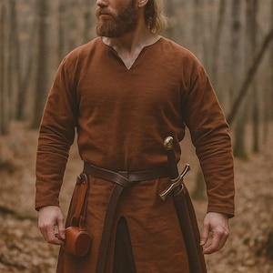 May include: A brown tunic with a V-neck, long sleeves, and a split front, worn with a brown leather belt and a sword in a sheath. A small leather pouch hangs from the belt. The outfit is reminiscent of historical or fantasy attire.