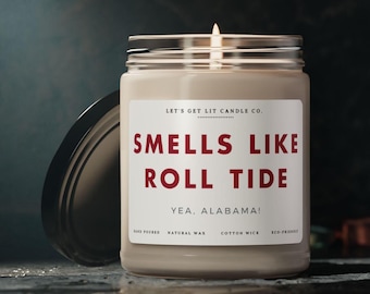 May include: A white candle jar with a black lid. The label reads "Let's Get Lit Candle Co." and "Smells Like Roll Tide Yea, Alabama!" with the words "Smells Like Roll Tide" in red. The jar is hand-poured, made with natural wax, has a cotton wick, and is eco-friendly.