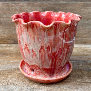 May include: A ceramic plant pot with a ruffled, scalloped rim and a matching saucer. The pot features a marbled glaze finish with swirling patterns of vibrant red, soft pink, and creamy white tones throughout the exterior surface.