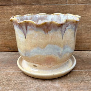 May include: A ceramic plant pot with a scalloped rim and a matching saucer. The pot features a reactive glaze with blended horizontal bands of cream, beige, and soft brown tones, creating a smooth, glossy finish with subtle color variations.