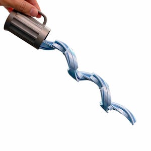 May include: A gray mug with a handle is tilted, seemingly pouring a stream of blue, ribbon-like material. The material twists and curves as it flows, creating a dynamic visual effect against a white background.