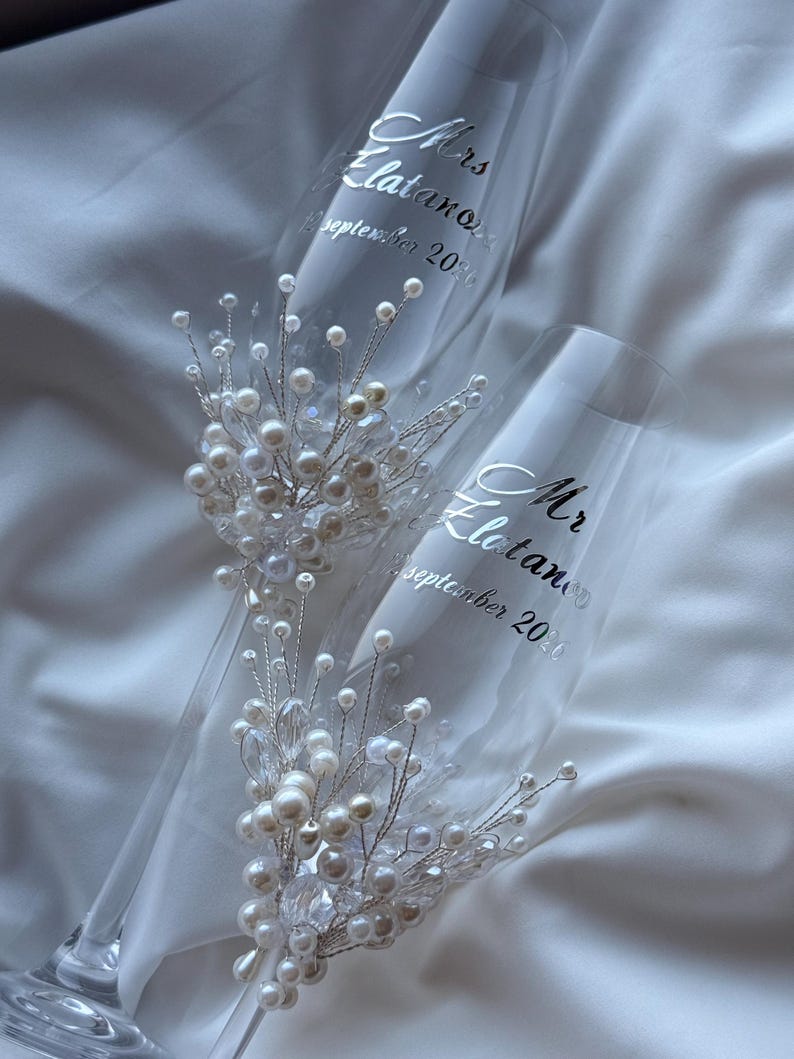 Puede incluir: Dos copas de champ&aacute;n con texto plateado "Mrs. Elatanov September 2020" y "Mr. Elatanov September 2020". Cada copa est&aacute; adornada con un delicado arreglo de perlas y cristales, creando un elegante tema de boda.