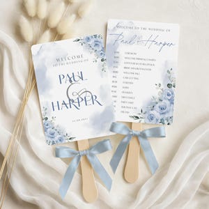 May include: Two wedding fan programs with light blue watercolor accents and floral details. The fans have wooden handles and light blue ribbon bows. The text reads "Welcome to the Wedding of Paul & Harper" and includes the date.