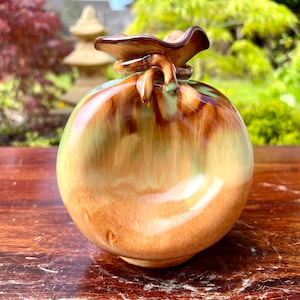 May include: A ceramic vase shaped like a brown and green sack with a knotted top.