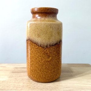 May include: A vintage ceramic vase with a two-tone design. The top half is a light tan color, while the bottom half is a textured, speckled brown. The vase has a cylindrical shape with a slightly flared rim, suitable for home decor.