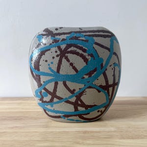 Op de afbeelding: Een set van drie keramische mokken met een gespikkelde, matte afwerking. De mokken zijn in crème, lichtgrijs en donkergrijs. Elke mok heeft een eenvoudig, minimalistisch ontwerp.