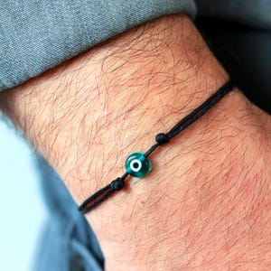 Puede incluir: Pulsera de cuerda negra con una cuenta de ojo turco verde y blanco. La pulsera está anudada y es ajustable. La pulsera se lleva en la muñeca.