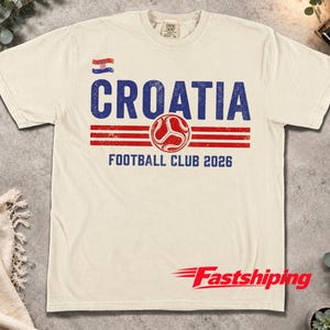 Peut inclure: Un t-shirt &agrave; manches courtes de couleur cr&egrave;me avec un motif vieilli bleu et rouge. Le design comprend un petit drapeau croate, le texte CROATIA, une ic&ocirc;ne de ballon de football et le texte FOOTBALL CLUB 2026 dans une police us&eacute;e.