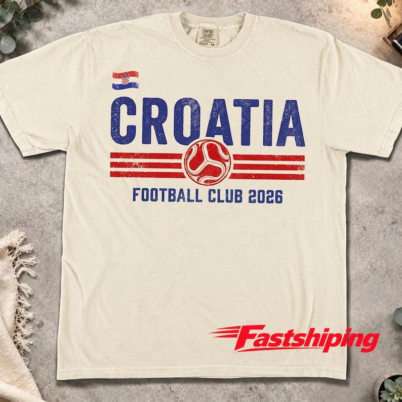 Peut inclure: Un t-shirt &agrave; manches courtes de couleur cr&egrave;me avec un motif vieilli bleu et rouge. Le design comprend un petit drapeau croate, le texte CROATIA, une ic&ocirc;ne de ballon de football et le texte FOOTBALL CLUB 2026 dans une police us&eacute;e.