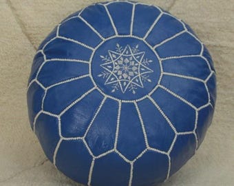 May include: Round blue leather ottoman with white stitching and a central snowflake design. The ottoman is a decorative piece, perfect for adding a touch of style to any living space. The ottoman is approximately 18 inches in diameter.