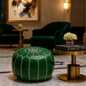 Pode incluir: Um pufe redondo de couro verde esmeralda com costuras brancas e um desenho de floco de neve na parte superior. O pufe está numa sala com cadeiras verde-escuras e uma pequena mesa lateral dourada. O texto "MorroDesign bywata" é visível.
