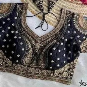 May include: Black embroidered top with gold accents and a V-neck design. The top features intricate patterns and embellishments, with a detailed border along the neckline and sleeves. The sleeves are short and adorned with similar gold embroidery.