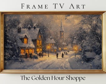 Op de afbeelding: Een ingelijst winterlandschapsschilderij met een gouden lijst. Het kunstwerk toont een besneeuwde dorpsstraat met verlichte gebouwen en straatlantaarns. De tekst "FRAME TV ART" en "The Golden Hour Shoppe" zijn zichtbaar.