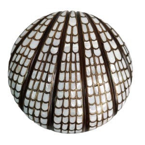 Op de afbeelding: Een decoratieve, ronde doos met een schelpachtig ontwerp. De doos heeft afwisselend donkerbruine en witte secties, met goudkleurige accenten. De algemene vorm is bolvormig en het ontwerp is ingewikkeld en gedetailleerd.