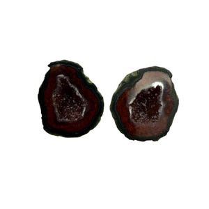 May include: Two geode halves with a dark red interior and a dark green and black outer edge. The interior has a crystalline structure. The geodes are displayed against a white background.