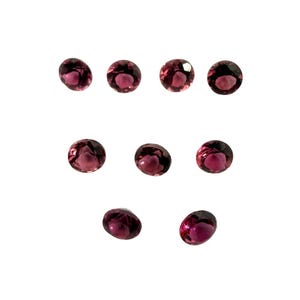 May include: Nine round, faceted, dark pink gemstones are arranged on a white background. The gems have a deep, rich color and a polished, reflective surface. The gemstones are likely for jewelry making.