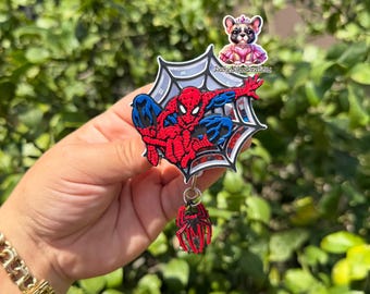 Puede incluir: Un portacredenciales con el personaje Spider-Man en rojo y azul sobre un fondo de telaraña blanca, con un elemento tipo shaker que contiene purpurina roja y azul. Un pequeño dije de araña roja cuelga en la parte inferior.