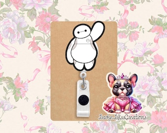 May include: A brown badge reel with a white and black Baymax character design. A second badge reel features a cartoon French Bulldog wearing a pink tutu and crown. The text "Badge Bliss Creations" is visible.