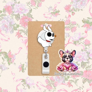 May include: A white retractable badge reel featuring Zero from The Nightmare Before Christmas, with a red collar and orange nose. A cartoon image of a French Bulldog wearing a pink dress and crown is also present. The text "Badge Bliss Creations" is visible.
