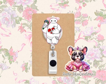 May include: A white retractable badge reel featuring a cartoon robot holding flowers and a heart. A small sticker of a French bulldog wearing a pink dress and crown is also included. The text "Badge Bliss Creations" is visible.