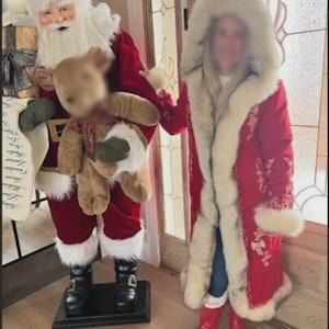 May include: A life-sized Santa Claus figurine wearing a red velvet suit with white faux fur trim, black boots, and a hat, holding a tan teddy bear and a scroll. Beside it, a long red coat with white faux fur trim and hood, and red boots.